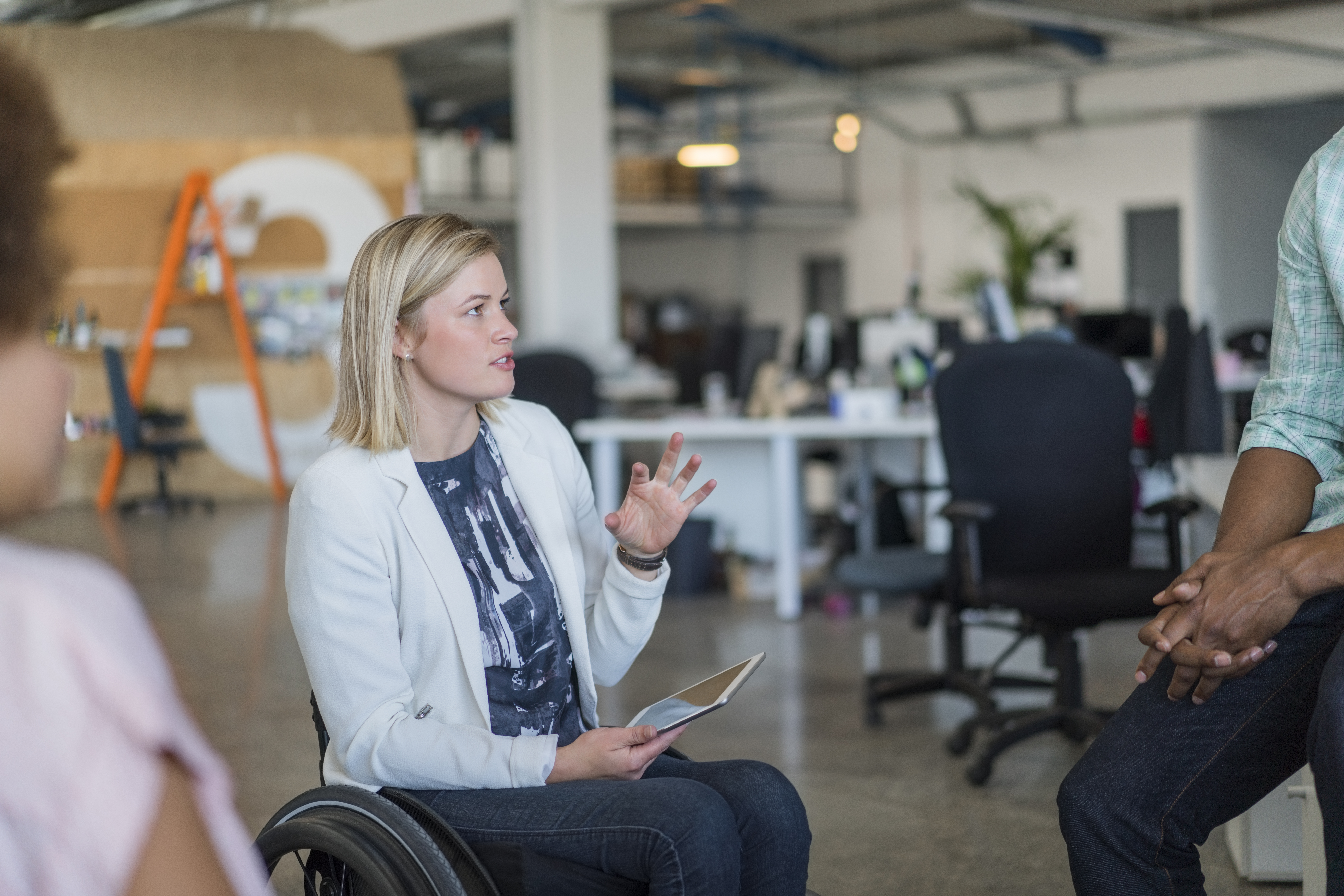 Empresaria discapacitada discutiendo con sus colegas en la oficina. Las profesionales femeninas están sosteniendo una tableta digital en una silla de ruedas. Los ejecutivos están reunidos en el lugar de trabajo.